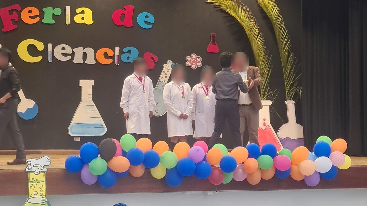 Estudiantes con mandil y un docente en el escenario durante la premiación