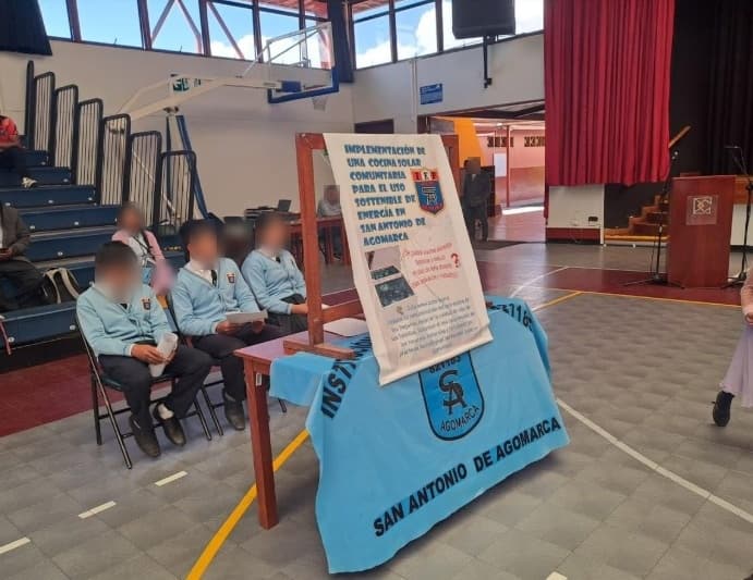 Estudiantes sentados junto al stand de la cocina solar comunitaria de la I.E. San Antonio de Agomarca